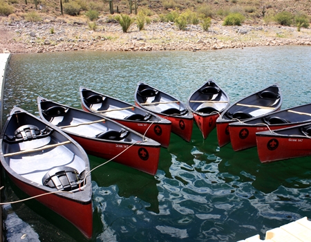 Seven bright red canoes floating on the water at the Desert Outdoor Center at Lake Pleasant.