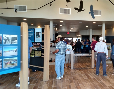 Visitors explore interactive exhibits inside the Discovery Center at Lake Pleasant Regional Park, with displays, informational panels, and overhead bird silhouettes.