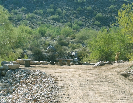 Stone benches line a dirt path along the Waterfall Trail at White Tank Mountain Regional Park, surrounded by desert vegetation and rocky terrain.