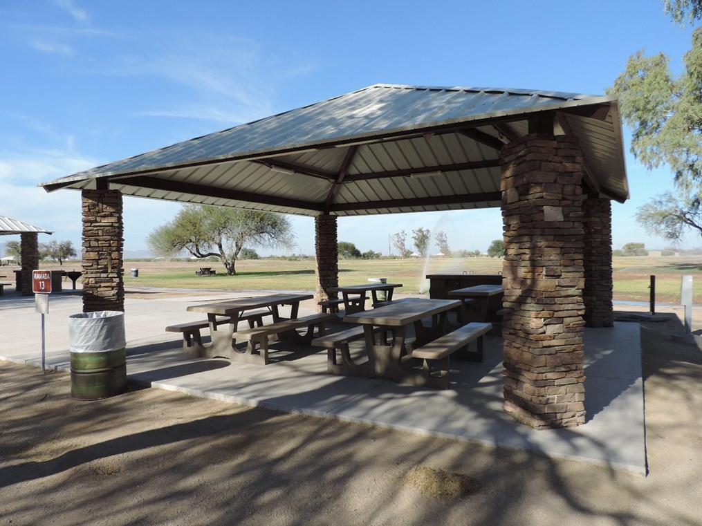Ramada 13 picnic shelter with metal roof, picnic tables on a cement slab, accessible walkway, and desert park setting