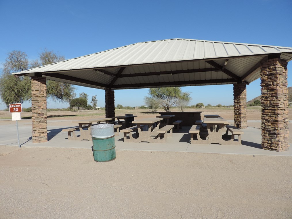 Ramada 20 picnic shelter with metal roof, picnic tables on a cement pad, accessible walkway, and open grassy area.