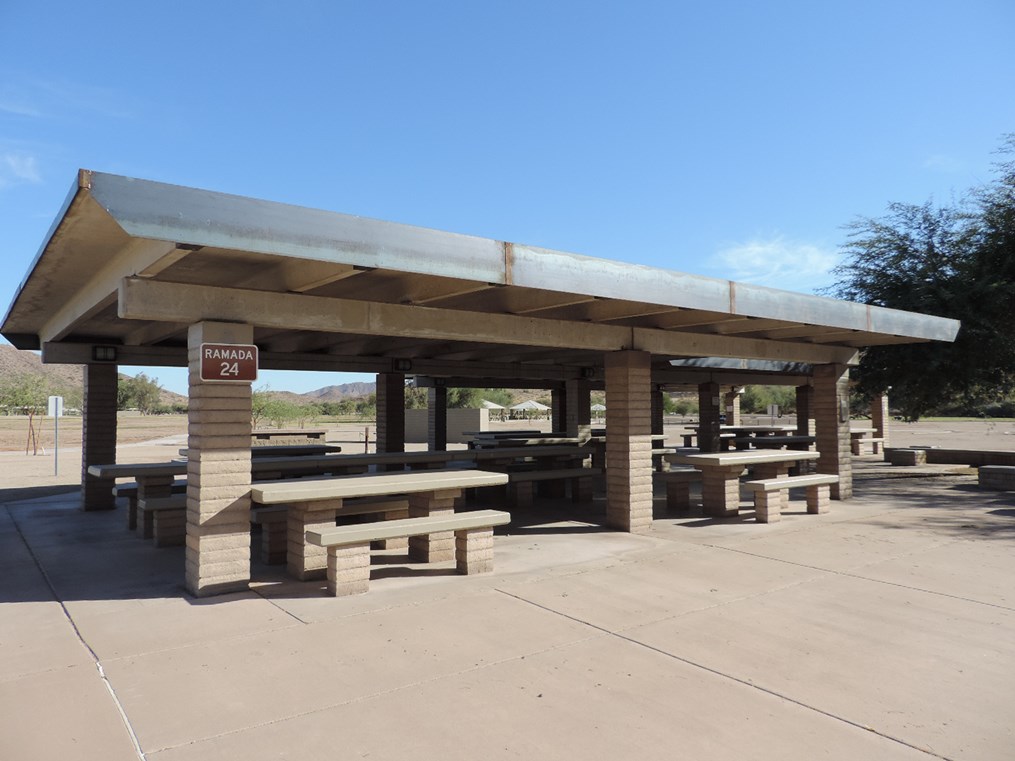 Ramada 24 large covered picnic complex with multiple tables on a cement slab and open park surroundings.