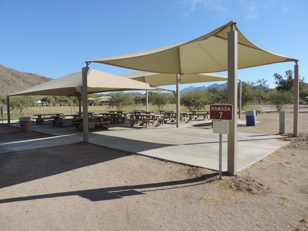 Ramada 7 shade-covered picnic area with tables on a cement pad and accessible sidewalk connection.