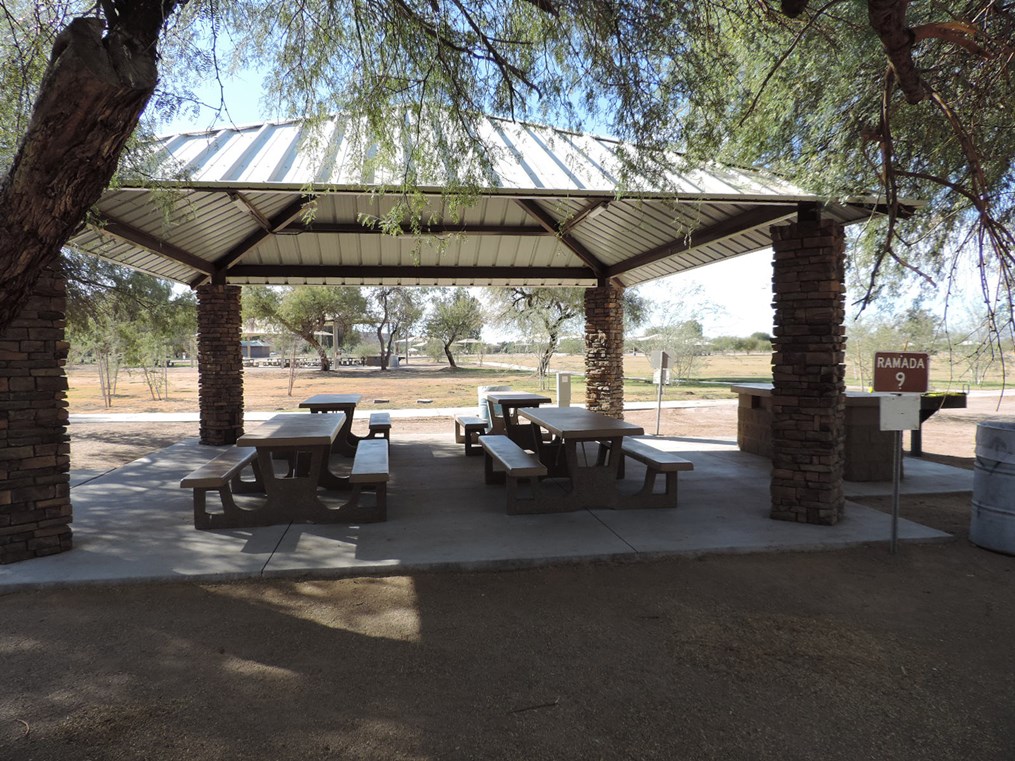 Ramada 9 picnic shelter with metal roof, picnic tables on a cement slab, accessible path, and shaded seating area.