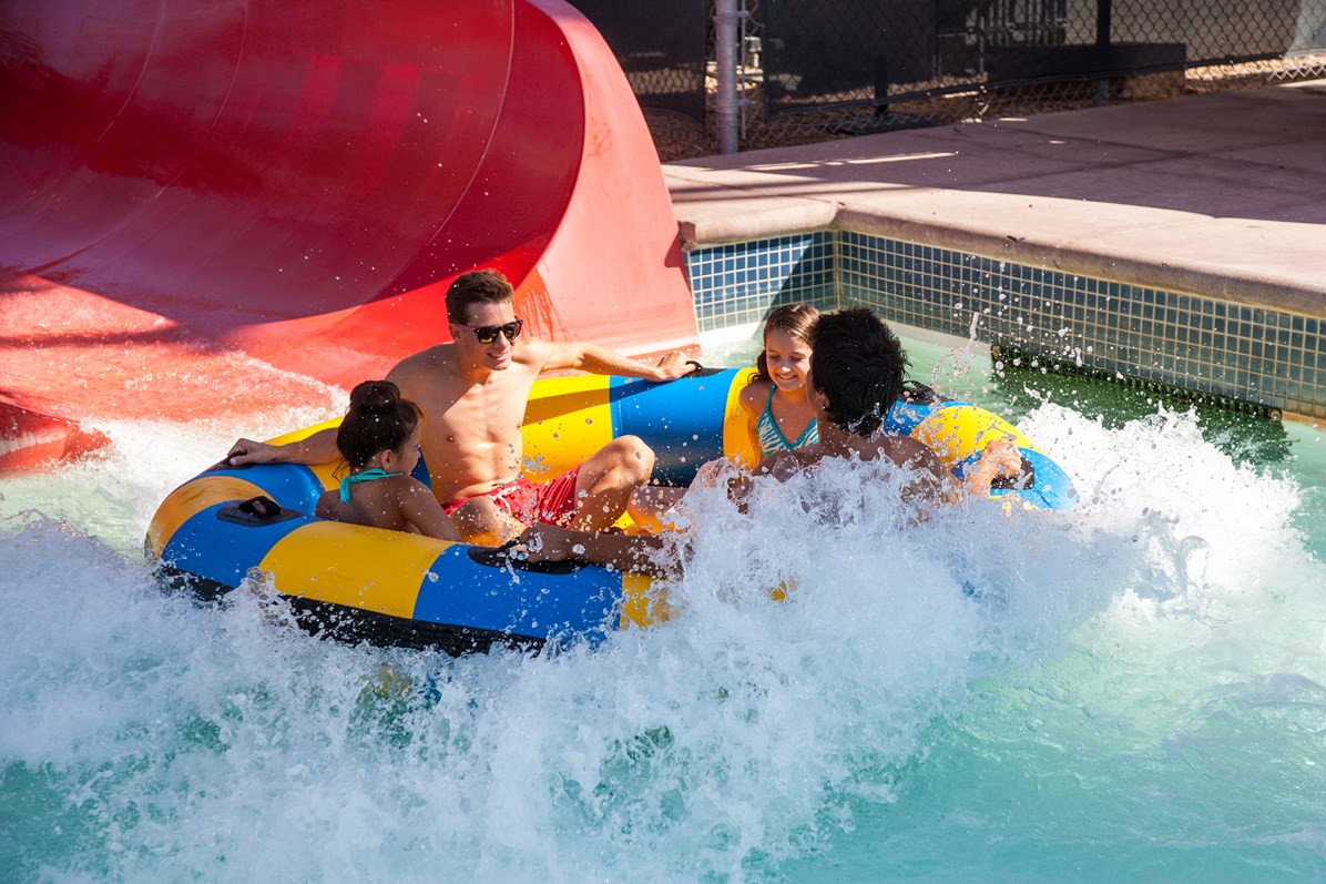 Adobe Dam - A family of four riding a giant tube down a slide and splashing into a pool of water.
