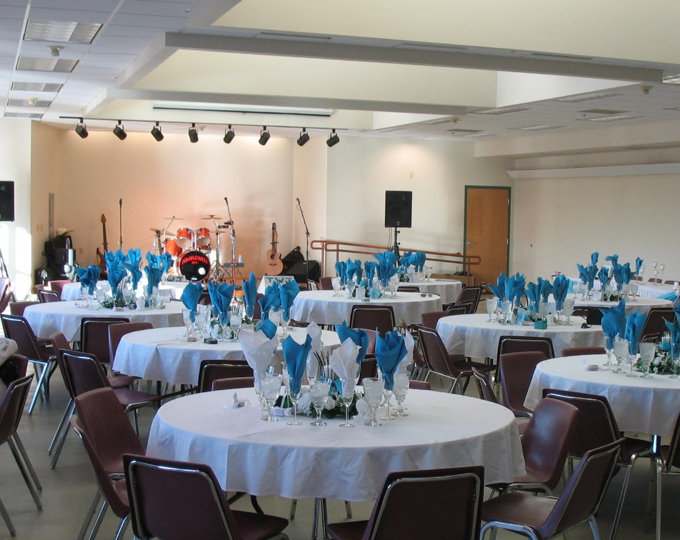 Event space set up with round tables, white tablecloths, blue napkins, and stage area with musical instruments and speakers.