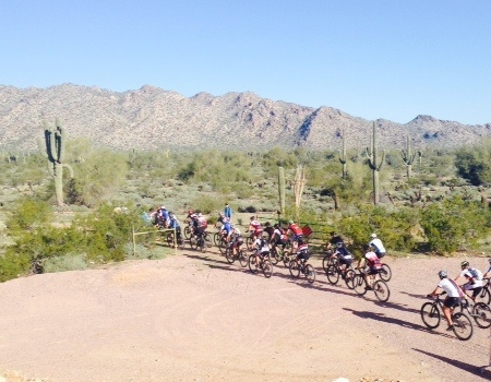 A group of mountain bikers rides along a desert trail at White Tank Mountain Regional Park with mountains and saguaro cacti in the background.