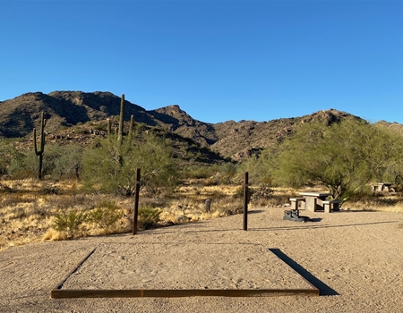 A campsite at Willow Campground in White Tank Mountain Regional Park with a picnic table, open space for tents, and desert mountains in the background.