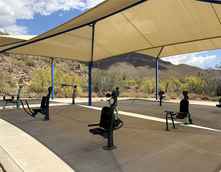 Outdoor fitness area at Usery Mountain Regional Park with exercise equipment set under a large shade canopy and desert mountains in the background.